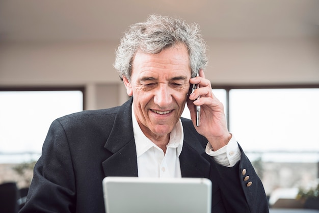 Free photo smiling senior man using mobile phone and digital tablet in the office