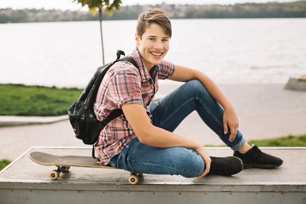 Бесплатное фото Улыбающийся подросток, сидя на скейтборде на барьер