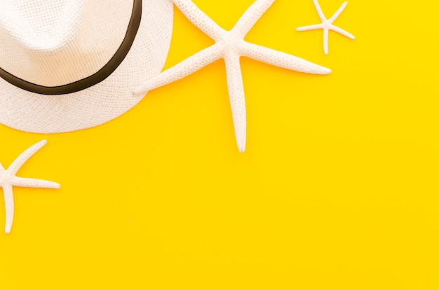 Бесплатное фото Соломенная шляпа с морскими звездами на желтом столе