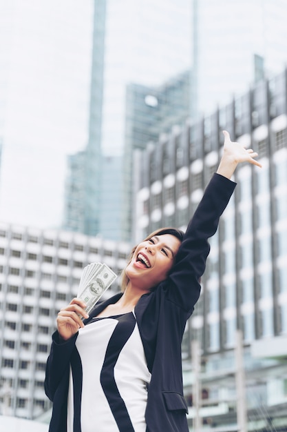 Бесплатное фото Успешная красивая азиатская бизнес-леди держа деньги долларовые банкноты в руке, концепцию дела