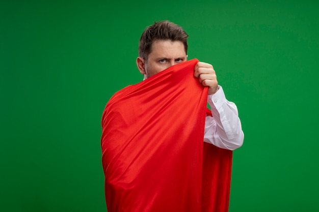 Бесплатное фото Бизнесмен супергероя, завернутый в красный плащ, смотрит в камеру с серьезным лицом, стоящим на зеленом фоне