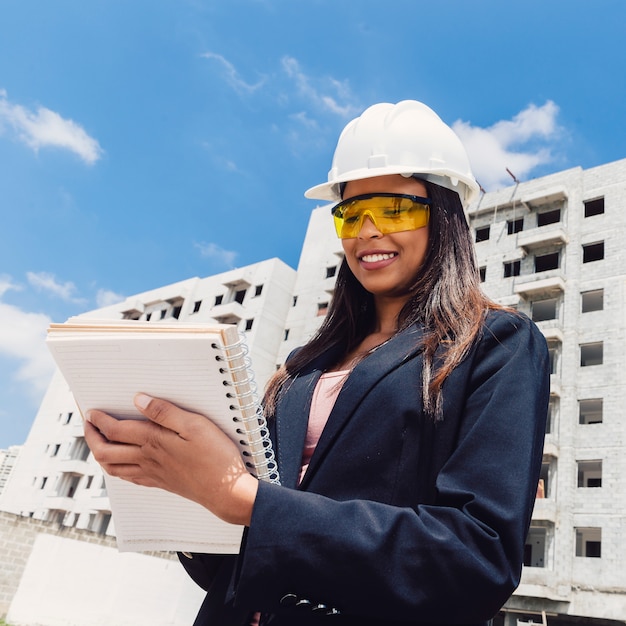 Photo gratuite afro-américaine dans un casque de sécurité avec un ordinateur portable près du bâtiment en construction