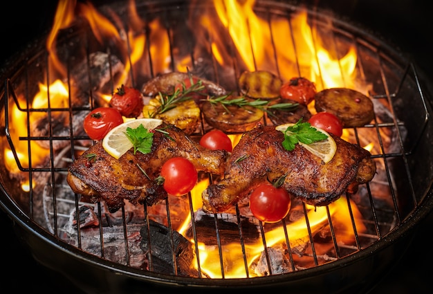 Photo gratuite cuisses de poulet grillées sur le gril flamboyant avec légumes grillés avec tomates, pommes de terre, graines de poivre, sel.