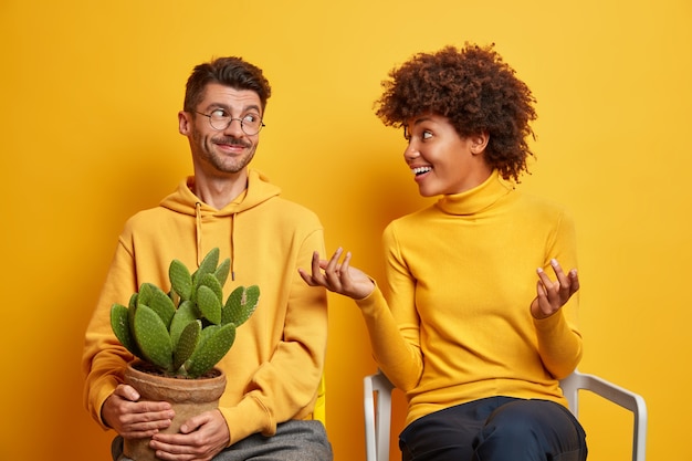 Photo gratuite une femme fait des gestes activement et parle avec son mari discuter de quelque chose essaie d'expliquer son idée déménager dans un nouvel appartement pose sur des chaises en jaune