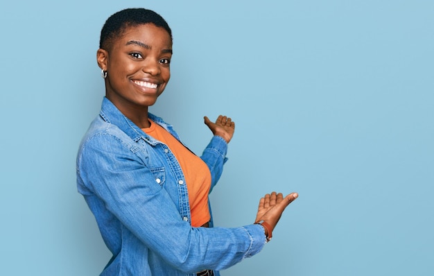 Photo gratuite jeune femme afro-américaine portant des vêtements décontractés invitant à entrer souriant naturel avec la main ouverte