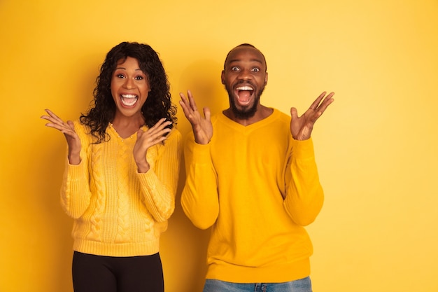 Photo gratuite jeune homme afro-américain émotionnel et femme en vêtements décontractés lumineux posant sur l'espace jaune. beau couple