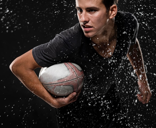 Joueur de rugby masculin avec ballon et éclaboussures d'eau