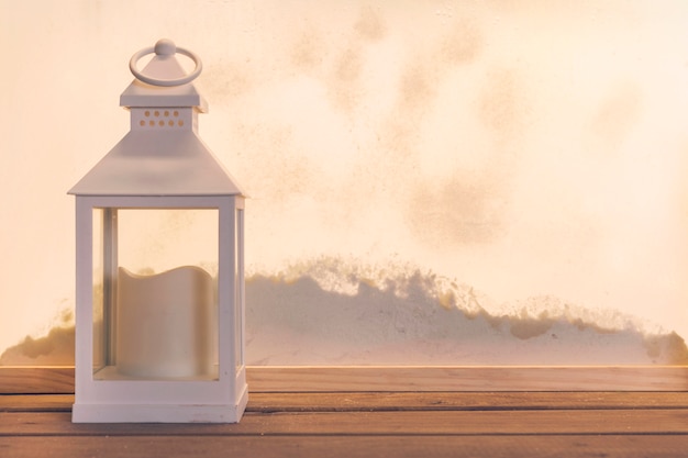 Photo gratuite lanterne avec bougie sur planche de bois près de tas de neige par la fenêtre