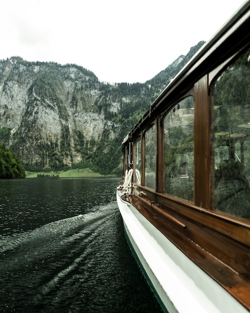 Photo gratuite tir vertical du bateau naviguant sur l'eau avec des montagnes boisées au loin
