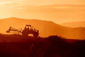 Photo gratuite tracteur dans un champ agricole au coucher du soleil. rétroéclairage tons chauds