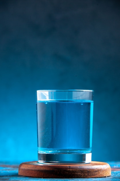 Photo gratuite vue de dessus d'une eau plate dans un verre sur une planche à découper en bois sur fond bleu
