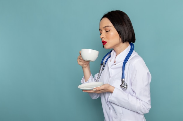 Photo gratuite une vue de face jeune infirmière en costume médical blanc et stéthoscope bleu buvant du thé