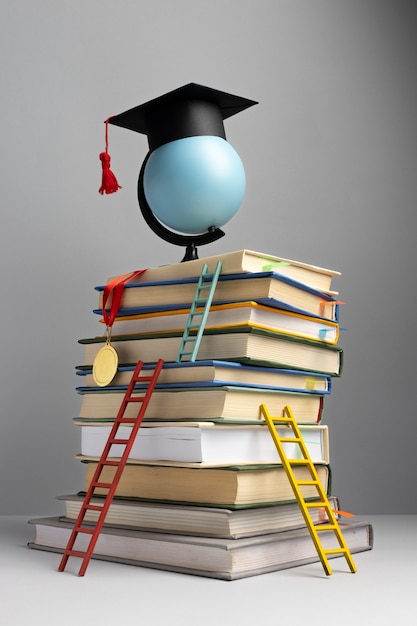 Photo gratuite vue de face de livres empilés, d'un chapeau de graduation et d'échelles pour la journée de l'éducation