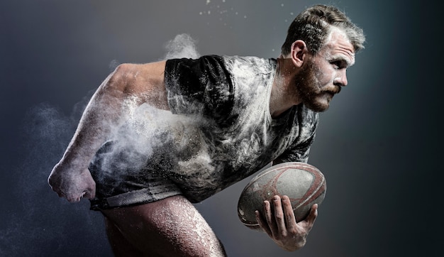 Vue latérale du joueur de rugby masculin athlétique tenant le ballon avec de la poussière