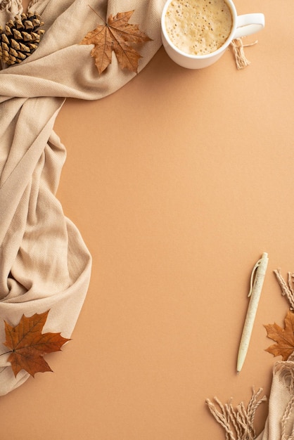 Photo concept d'entreprise d'automne vue de dessus photo verticale d'une tasse de travail mousseuse de boissons chaudes tombées feuilles d'érable stylo et écharpe de cône de pin sur fond beige isolé