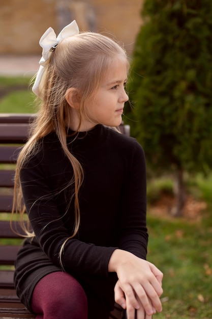 Photo une belle fille blonde aux cheveux longs dans une robe noire est assise sur un banc de parc