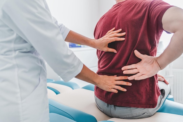 Gros plan recadré d'une orthopédiste examinant le dos du patient à la clinique