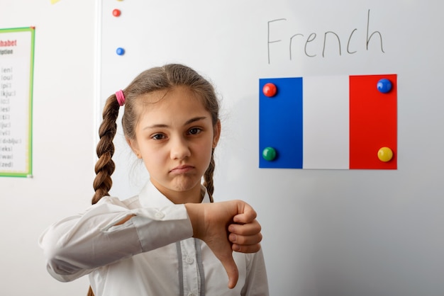 Écolière montrant les pouces vers le bas à la salle de classe avec un drapeau français au tableau