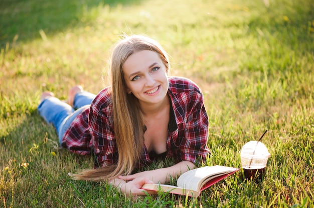 Photo fille boire du jus et lire un livre dans un parc.
