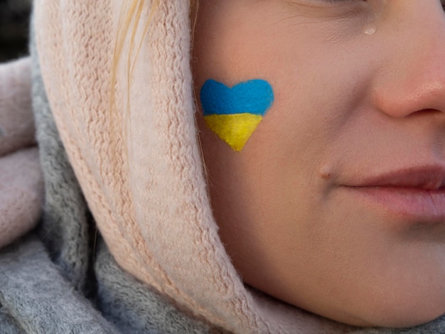 Fille qui pleure avec un drapeau ukrainien bleu-jaune en forme de cœur sur sa joue S'il vous plaît, arrêtez la guerre, sauvez-nous