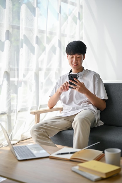Un homme asiatique utilise son smartphone pour discuter avec ses amis tout en restant à la maison