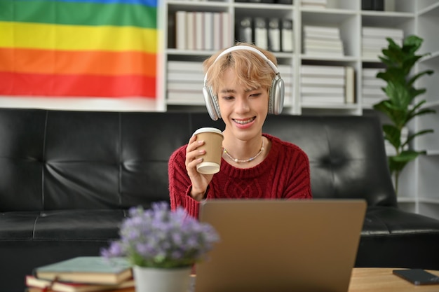 Un homme gay asiatique heureux sirote un café et lit quelque chose sur le site Web sur son ordinateur portable