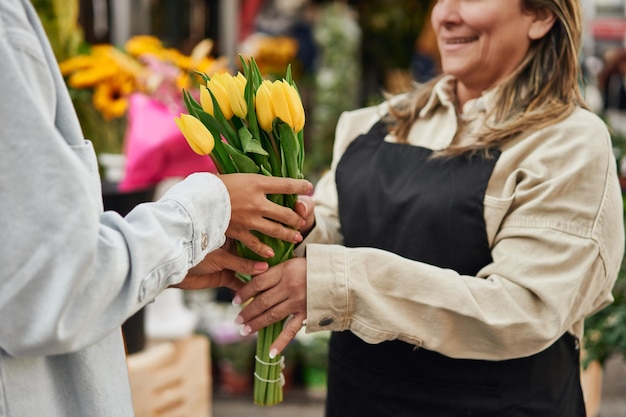 Jeune femme latina achetant des fleurs et des plantes vibrantes à l'étal d'un vendeur de rue