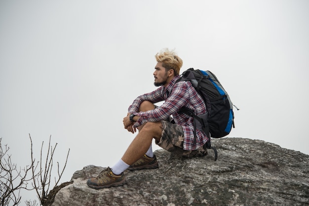 Photo jeune hipster hiker avec un sac à dos assis sur le sommet de la montagne.