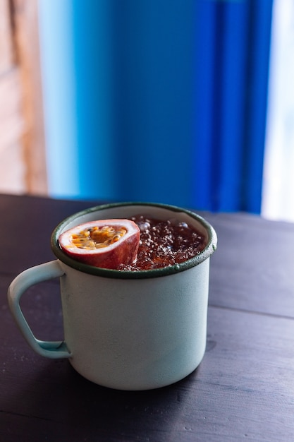 Photo jus de fruit glacé passion servi dans une tasse de zinc avec une moitié coupée de fruit de la passion frais.