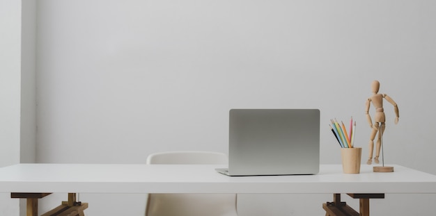 Ordinateur portable sur une table blanche et une tasse de café dans une salle de bureau moderne avec un mur blanc