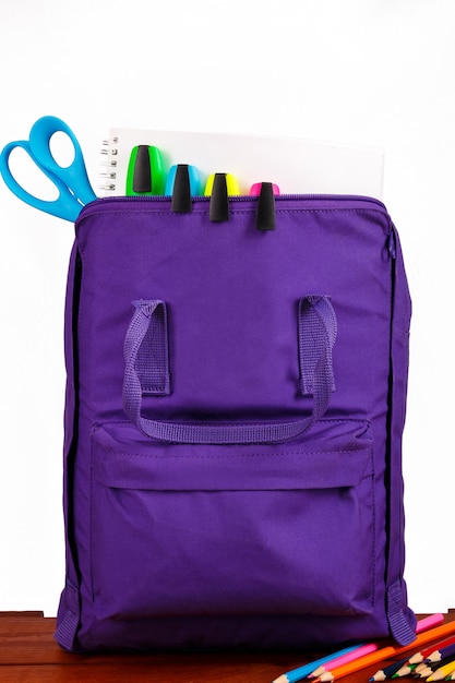 Photo ouvrir le sac à dos violet avec des fournitures scolaires sur la table en bois. retour à l'école.