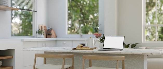 Une maquette d'ordinateur portable sur un îlot de cuisine moderne ou un comptoir de cuisine dans une cuisine blanche moderne
