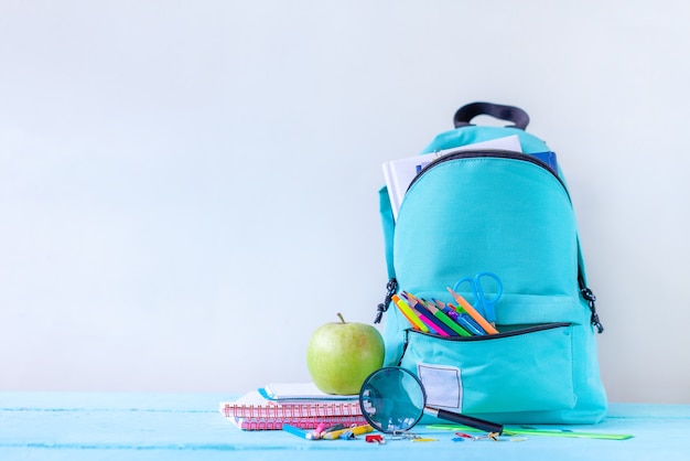 Photo sac à dos scolaire turquoise avec papeterie sur table.