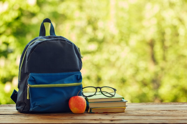 Photo sac à dos scolaire avec des livres sur table en bois et fond de nature