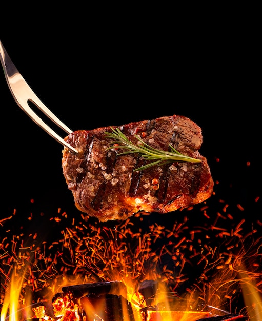 Photo steak de boeuf tombant sur le gril avec le feu.