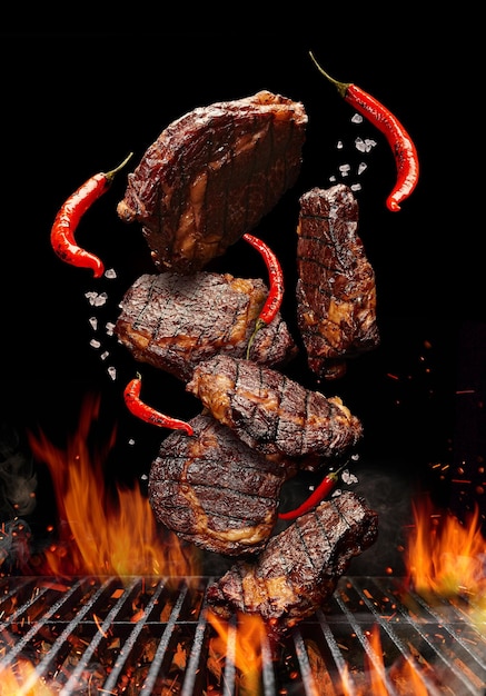 Photo des steaks de porc ou de bœuf grillés avec du piment et du sel tombent sur un barbecue à fond noir...