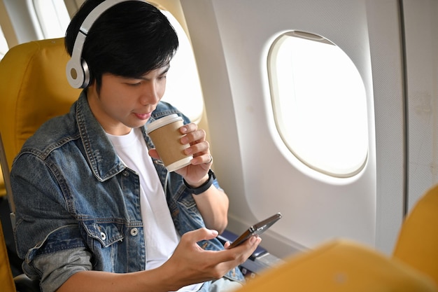 Passager masculin asiatique écoutant de la musique à travers ses écouteurs pendant le vol