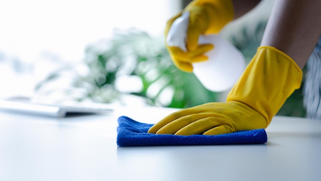 Photo la personne qui nettoie le personnel de nettoyage de la chambre utilise un chiffon et pulvérise du désinfectant pour essuyer les tables dans le bureau de l'entreprise personnel de nettoyage maintien de la propreté dans l'organisation