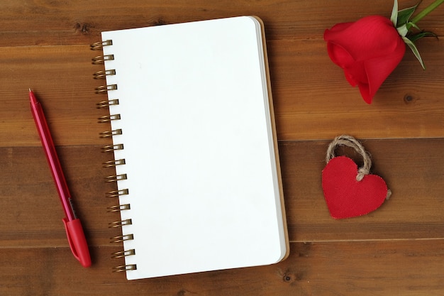 Photo rose rouge, forme de coeur de tissu et papier blanc carnet de notes sur fond de bois