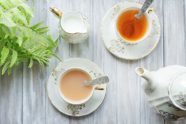 Photo thé anglais traditionnel à cinq heures dans un élégant ensemble de porcelaine. deux tasses de thé et de lait sur un plateau vintage en bois. mise à plat.