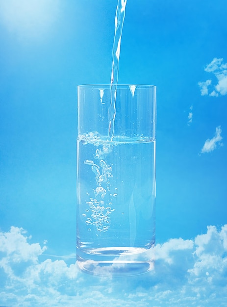 Photo verser de l'eau dans un verre contre un ciel bleu avec des nuages