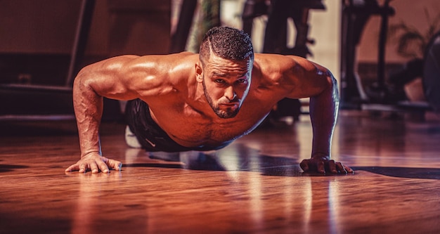 Mężczyzna robiący pompki Muskularny i silny facet ćwiczący Muskularna mężczyzna robiąca pompki Szczupły mężczyzna robijący pompki w siłowni