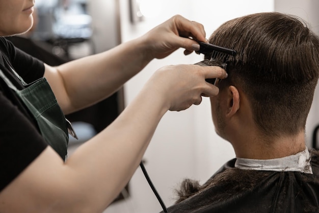 Mężczyzna strzyże włosy na skroniach maszynką do strzyżenia włosów w salonie fryzjerskim