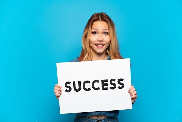 Zdjęcie nastoletnia dziewczyna trzyma afisz z tekstem sukces ze zdziwionym wyrazem na odosobnionym niebieskim tle