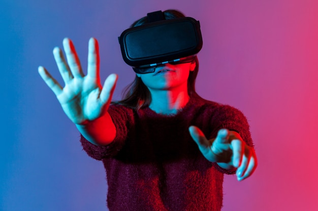 Kobieta w okularach VR stoi wyciągniętymi rękami, wybiera wirtualne menu, przycisk kliknięcia, gra w symulator gry, przeżywa cyberprzestrzeń. Innowacja, koncepcja technologii. strzał studio światła neonowego