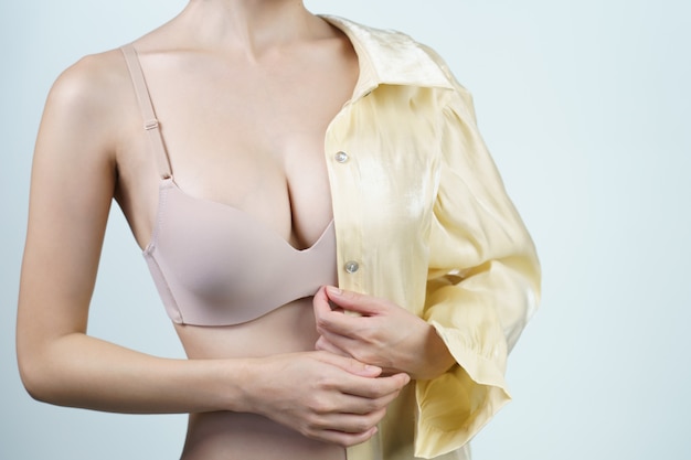 Zdjęcie kobieta zdejmuje jasnożółtą koszulę, jest w lekkiej nagiej bieliźnie. koncepcja operacji implantu piersi.