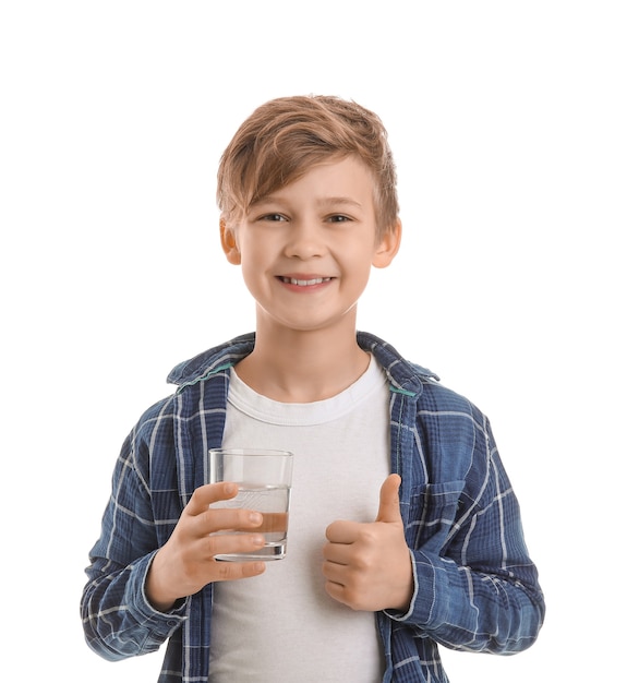 Ładny mały chłopiec ze szklanką wody pokazując kciuk w górę na białym tle
