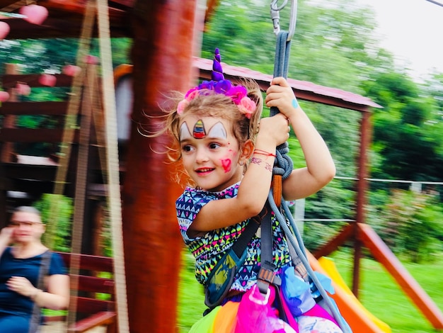 Zdjęcie słodka dziewczyna z kolorową farbą na twarzy wisząca na przejażdżce w parku rozrywki