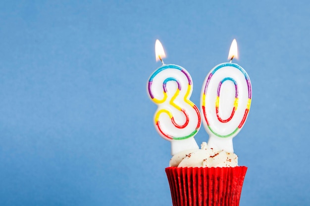 Zdjęcie urodzinowa świeczka numer 30 w babeczce na niebieskim tle