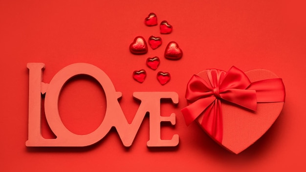 Walentynki lub wesele romantyczna koncepcja i słowo miłość. Czerwone świąteczne pudełko i czekoladki na czerwonym tle. Widok z góry, płaskie świecenie, kopia przestrzeń